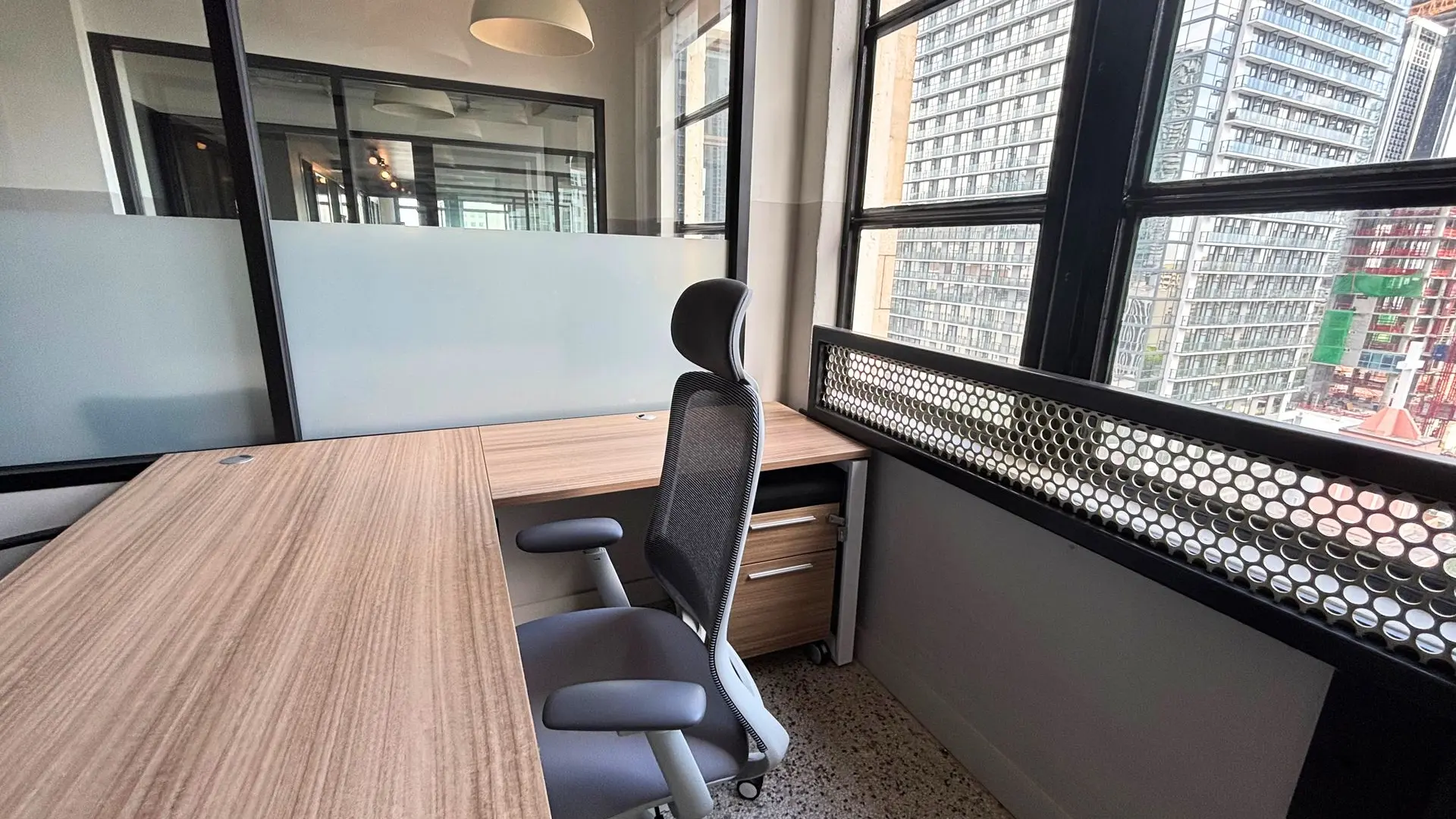 Private office with a wood desk, a grey mesh task chair and a glass wall with a perforated screen