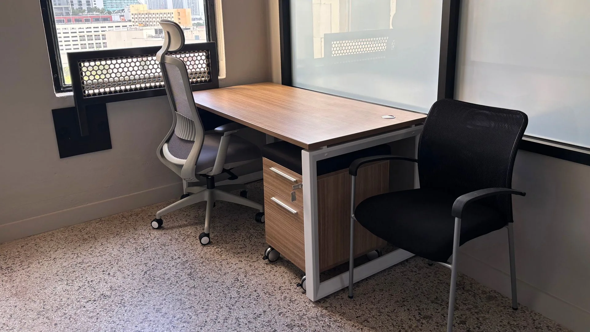 Private office with a wood desk, a black guest chair and a storage pedestal by a glass wall