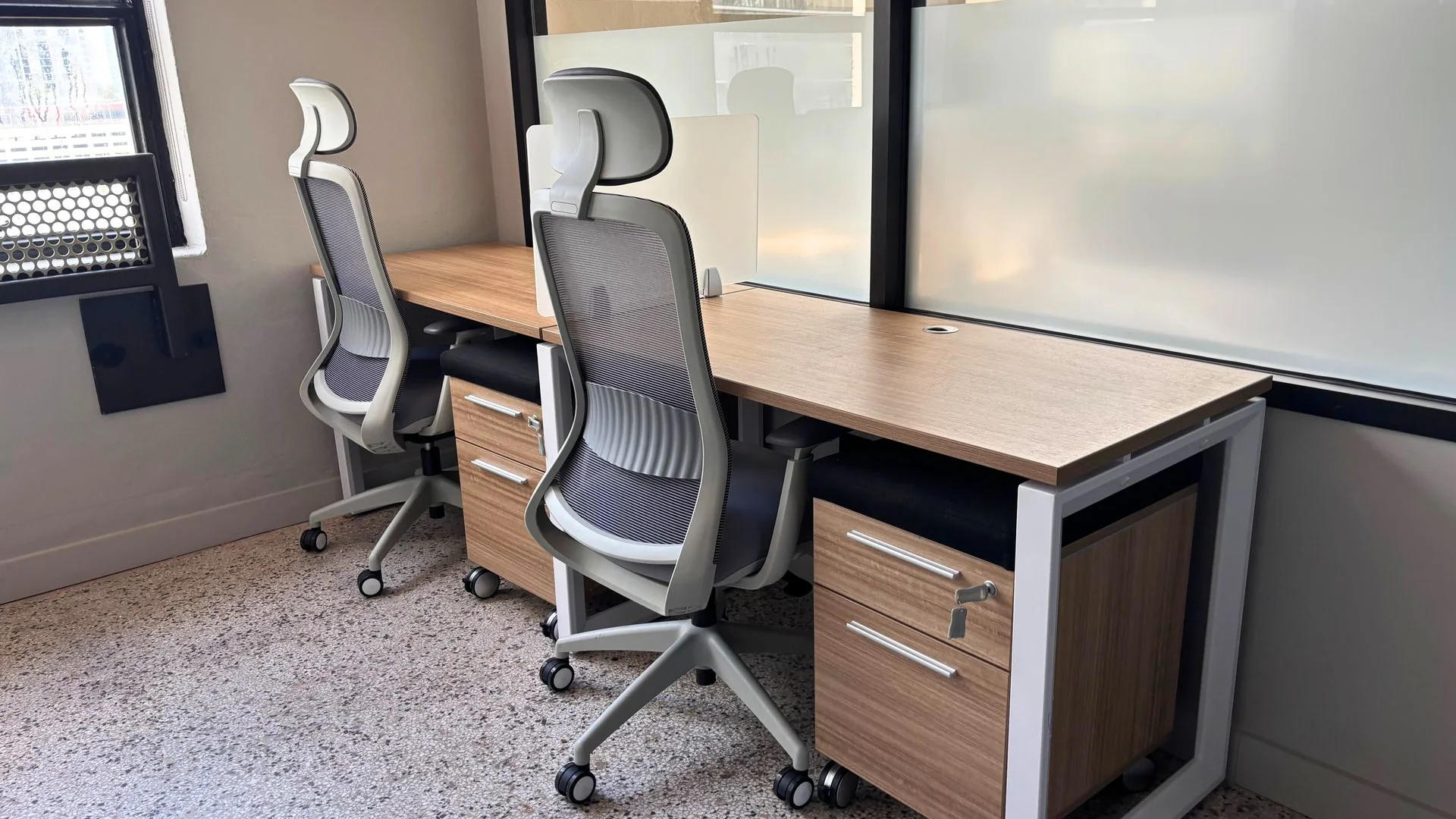 Private office with a wood desk, a grey task chair and a storage pedestal by a glass partition
