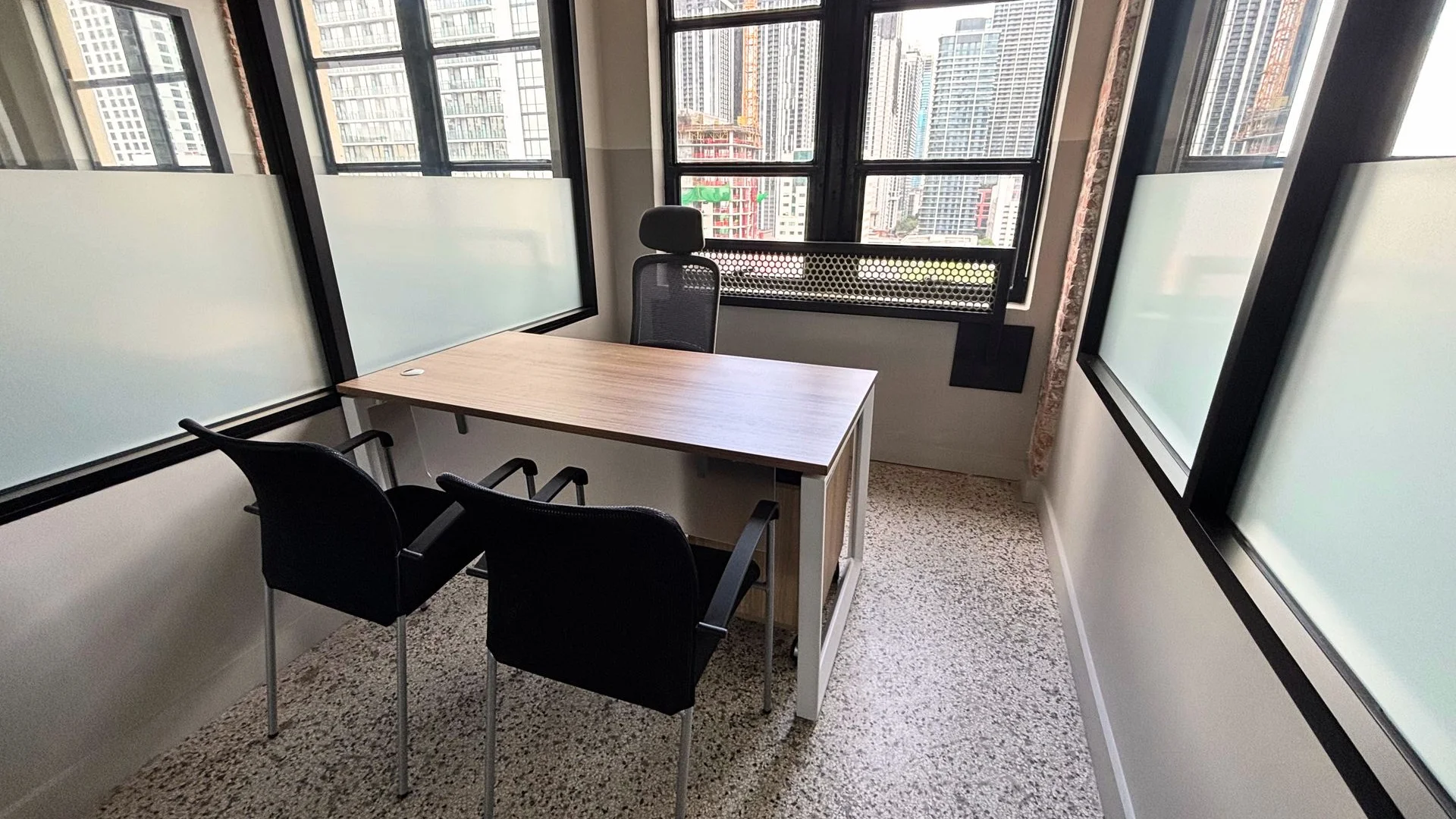 Finished private office with a wood desk, two black guest chairs and a glass partition by the windows