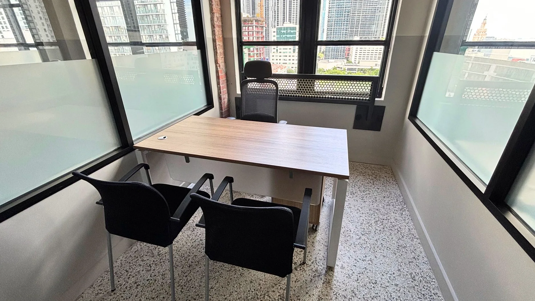 Private office with a wood table, two black guest chairs and a glass partition by the windows