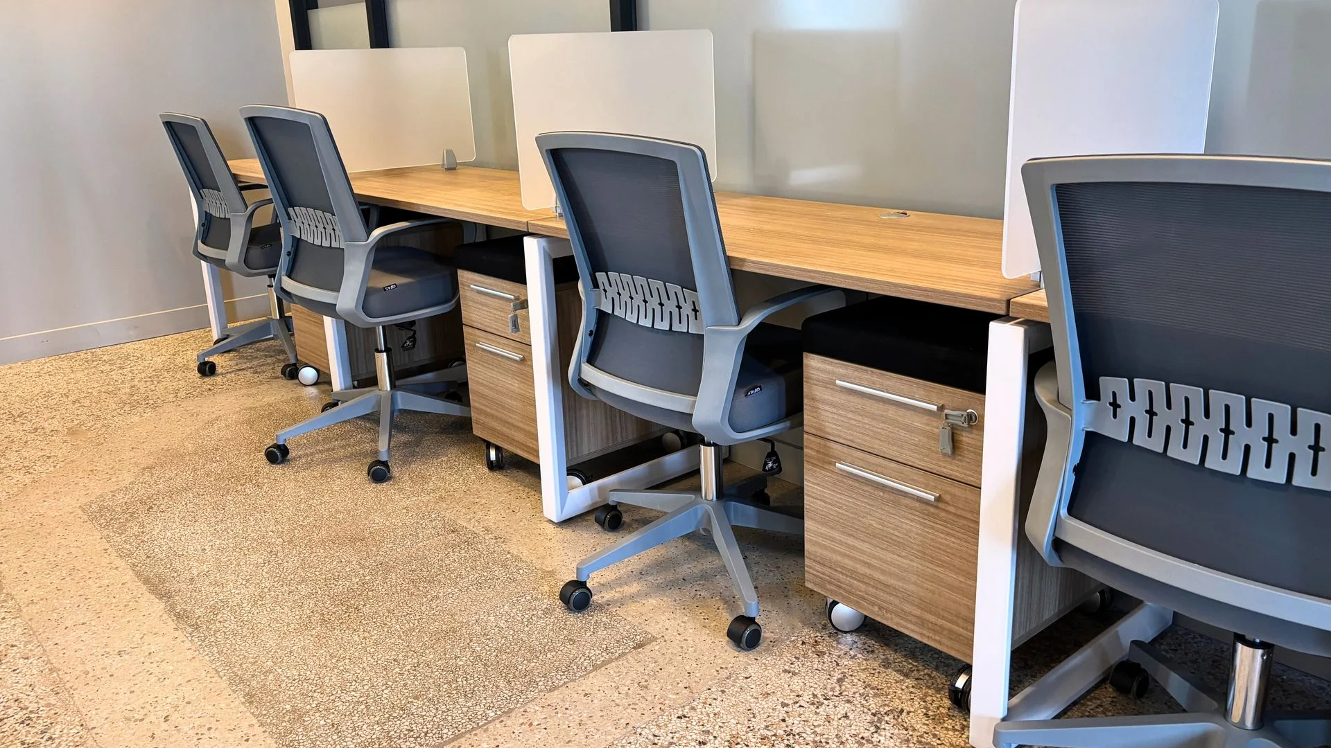 Workstation pod with wood desks, grey privacy screens, a storage pedestal and grey task chairs