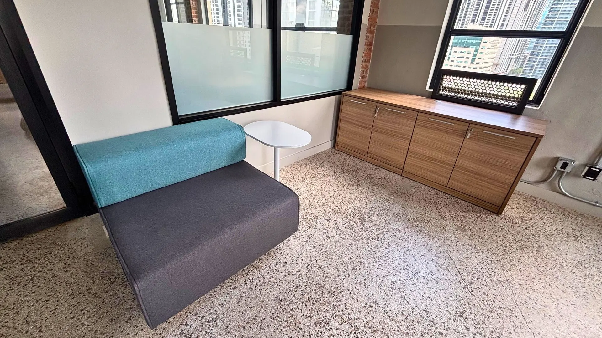 Lounge nook with a teal and grey upholstered bench, a round side table and a wood storage credenza