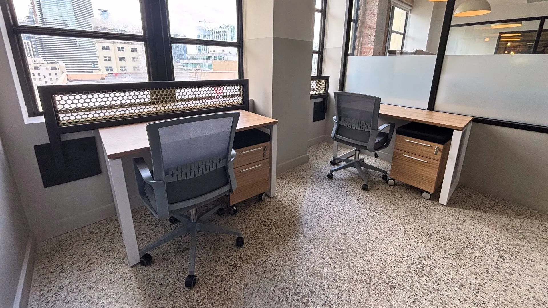 Private office with a wood desk, two black guest chairs and a glass wall with a perforated screen