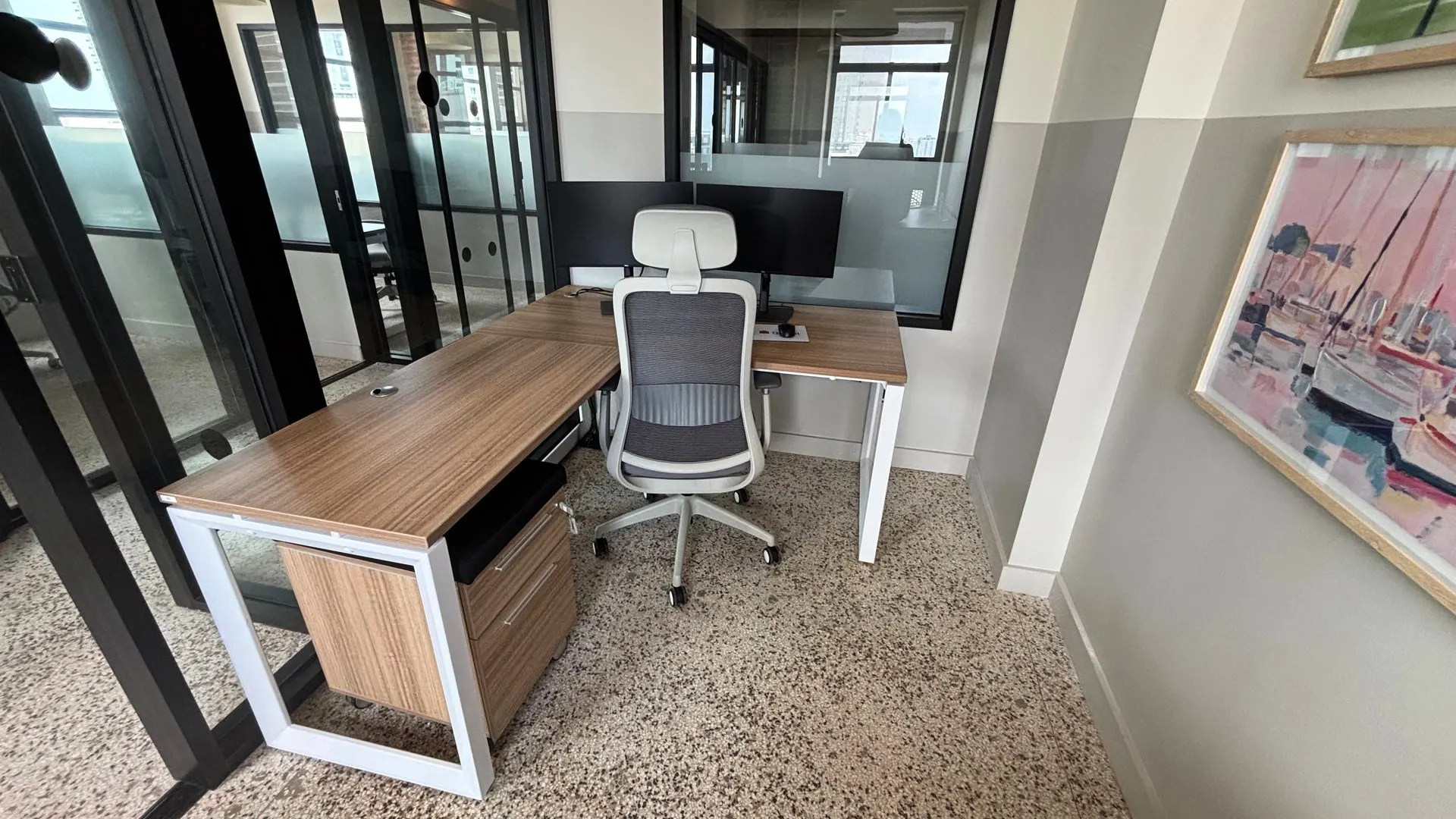 Private office with an L-shaped wood desk, a grey mesh task chair and framed art on the wall