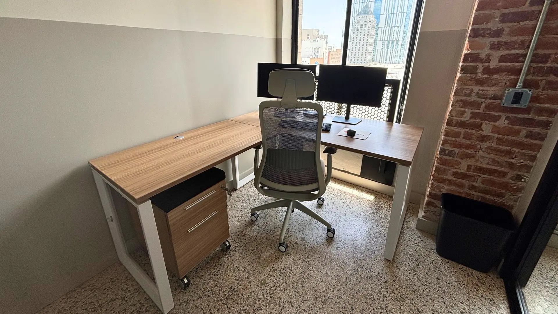 Private office with a wood desk, dual monitors, a grey task chair and a brick accent column