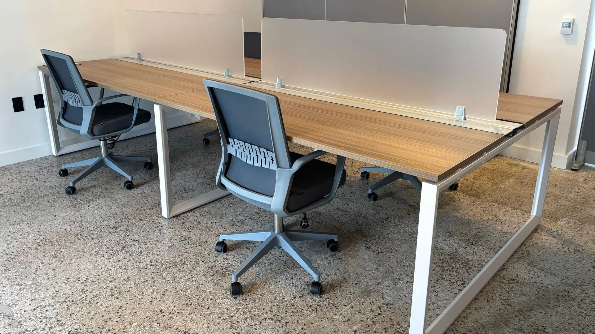 Shared bench workstations with wood tops, white frame legs and a grey task chair