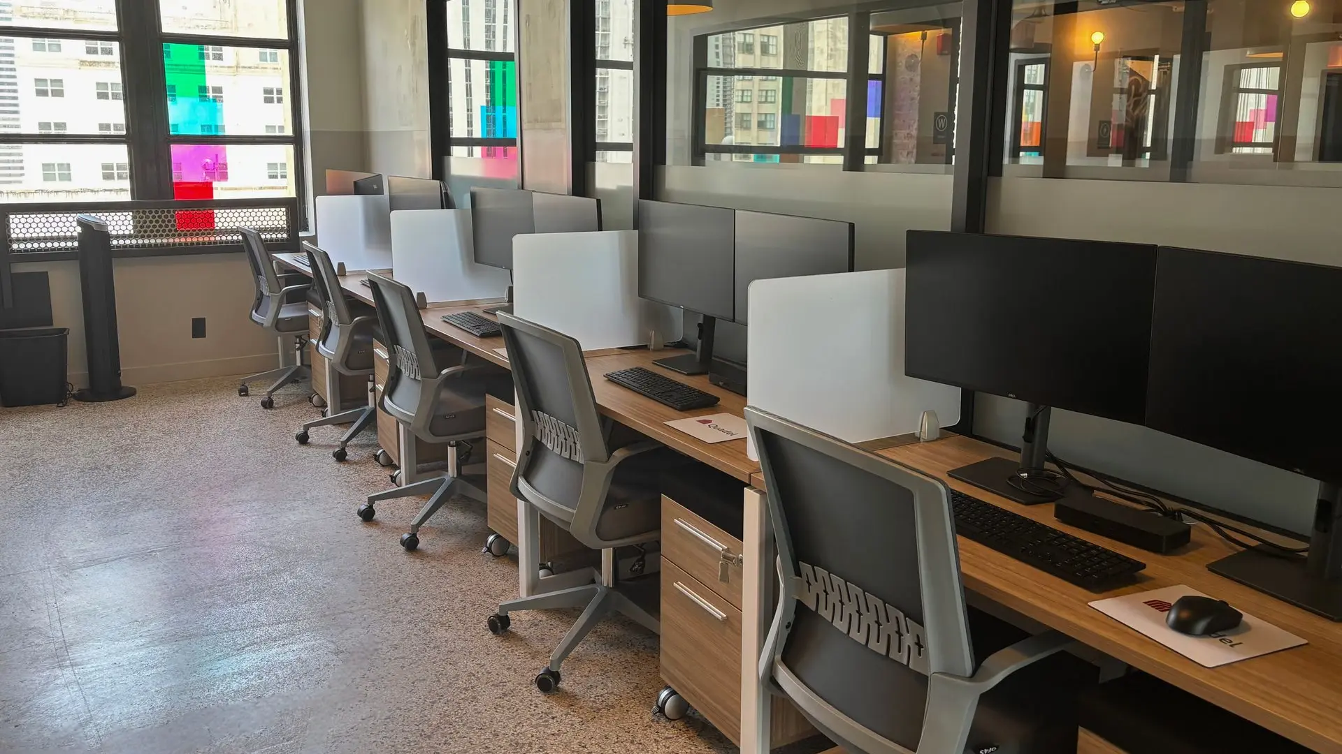 Workstation run with wood desks, grey privacy screens, monitors and grey task chairs