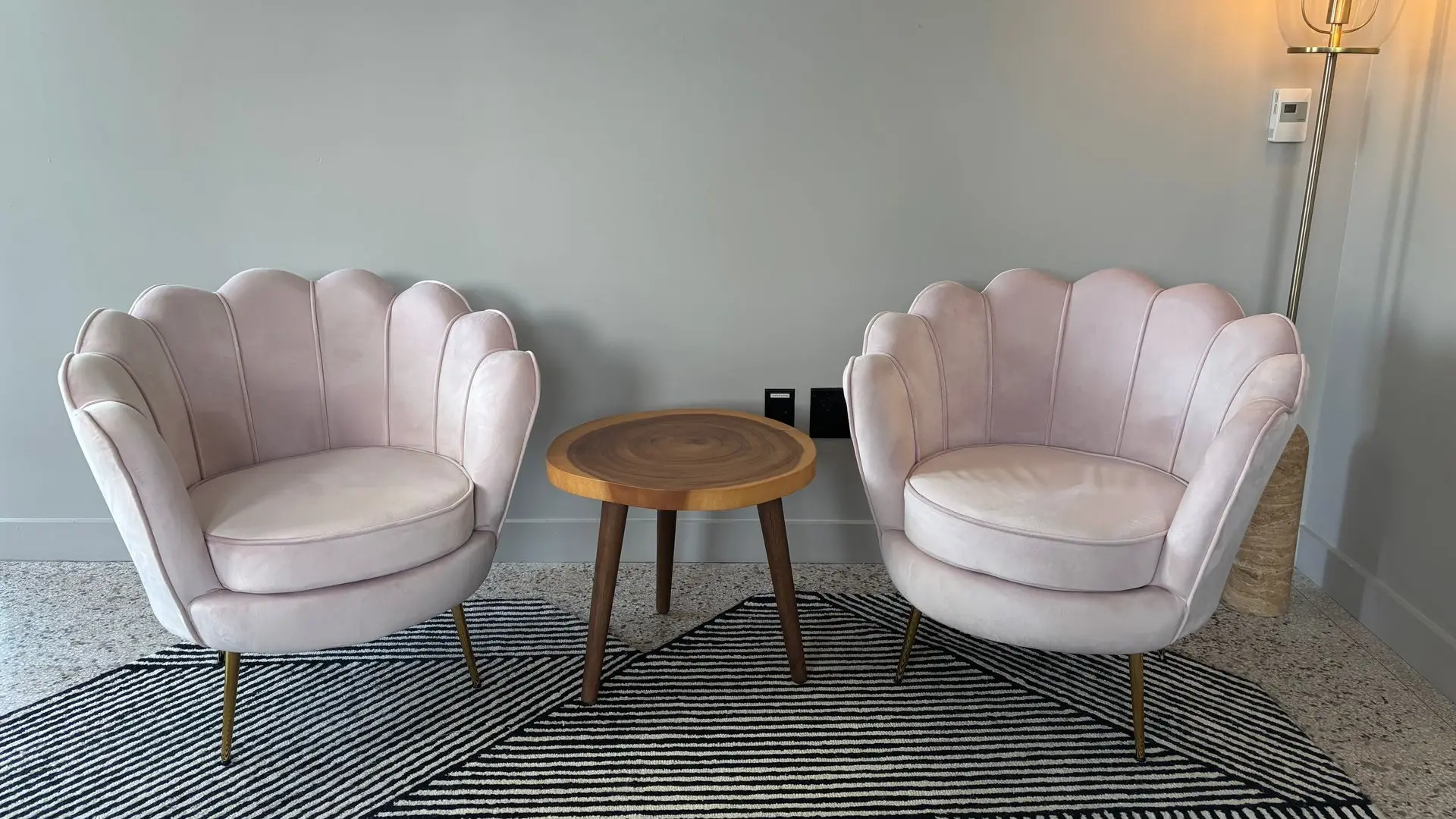 Waiting nook with two blush shell-back accent chairs and a small round wood side table on a patterned rug