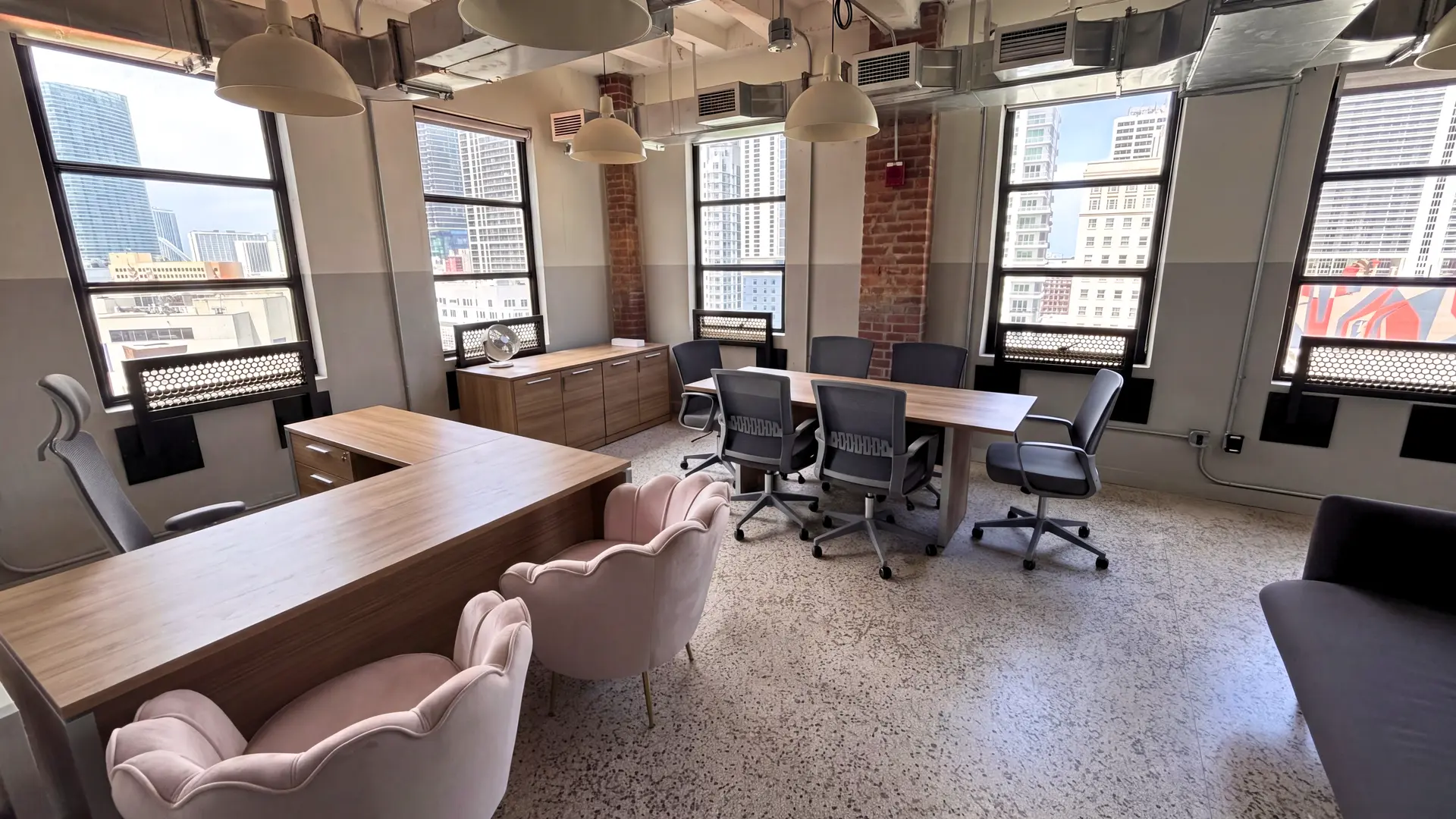 Welcoming reception and meeting area with a wood table, grey and blush accent chairs by a wall of windows