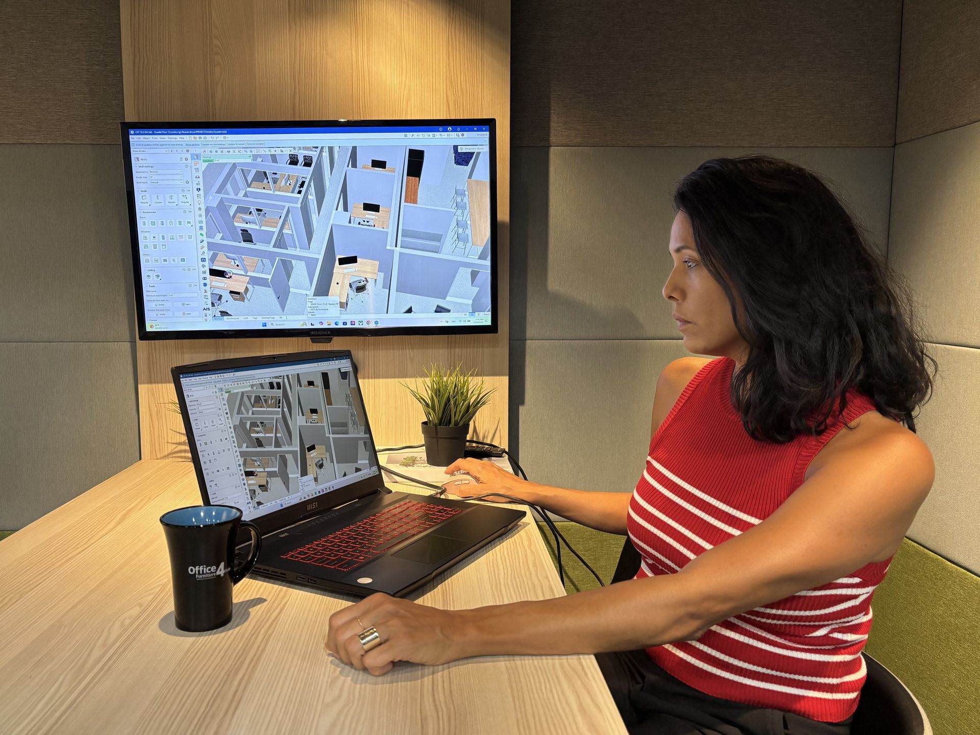 An OF4S designer reviewing the Quadel 3D office model on a wall monitor and a laptop